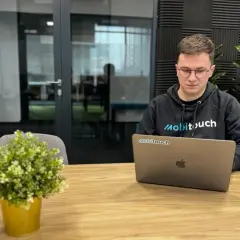 Młody programista w bluzie z logo "mobitouch" pracuje na laptopie. Zastanawia się, co to jest react, tworząc nowoczesne aplikacje.