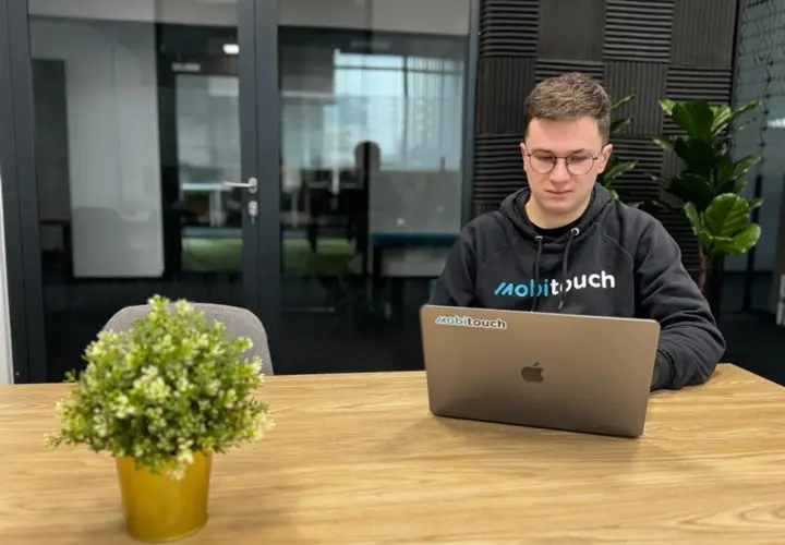 Młody programista w bluzie z logo "mobitouch" pracuje na laptopie. Zastanawia się, co to jest react, tworząc nowoczesne aplikacje.