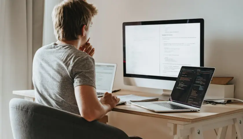 Młody programista pochyla się nad biurkiem, analizując kod na ekranach. Zastanawia się nad optymalizacją zapytań, wykorzystując funkcje agregujące SQL do efektywnego przetwarzania danych.