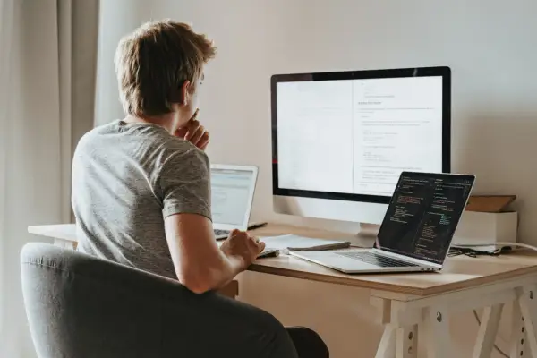 Młody programista pochyla się nad biurkiem, analizując kod na ekranach. Zastanawia się nad optymalizacją zapytań, wykorzystując funkcje agregujące SQL do efektywnego przetwarzania danych.